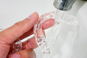 A person cleaning their Invisalign aligners with water